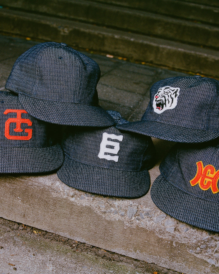 Five dark indigo-dyed dobby cotton Tokyo Giants 1940 Japanese Indigo Dobby Cotton Ballcap baseball caps with various embroidered logos stacked on concrete steps.