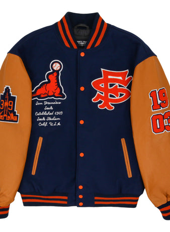 The Ebbets Field San Francisco Seals MiLB Dna Varsity Jacket features navy and tan colors with orange accents, chest patches like SF, 1903, a baseball graphic, San Francisco Seals text, and city/team details on the sleeves.