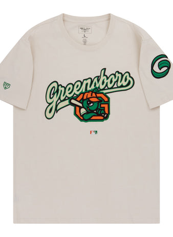 The Ebbets Field Greensboro Grasshoppers MiLB Fashion Cotton Short Sleeve Tee is a beige shirt with a bold Greensboro script, cartoon eye, and orange slices on the chest, plus green logos on the sleeves.