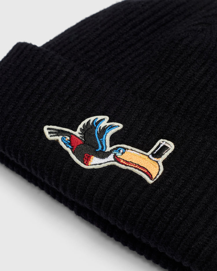 Guinness Flying Toucan Felt Patch Ribbed Beanie in black rib-knit, featuring an embroidered patch of a Guinness toucan flying with a glass of stout balanced on its beak.