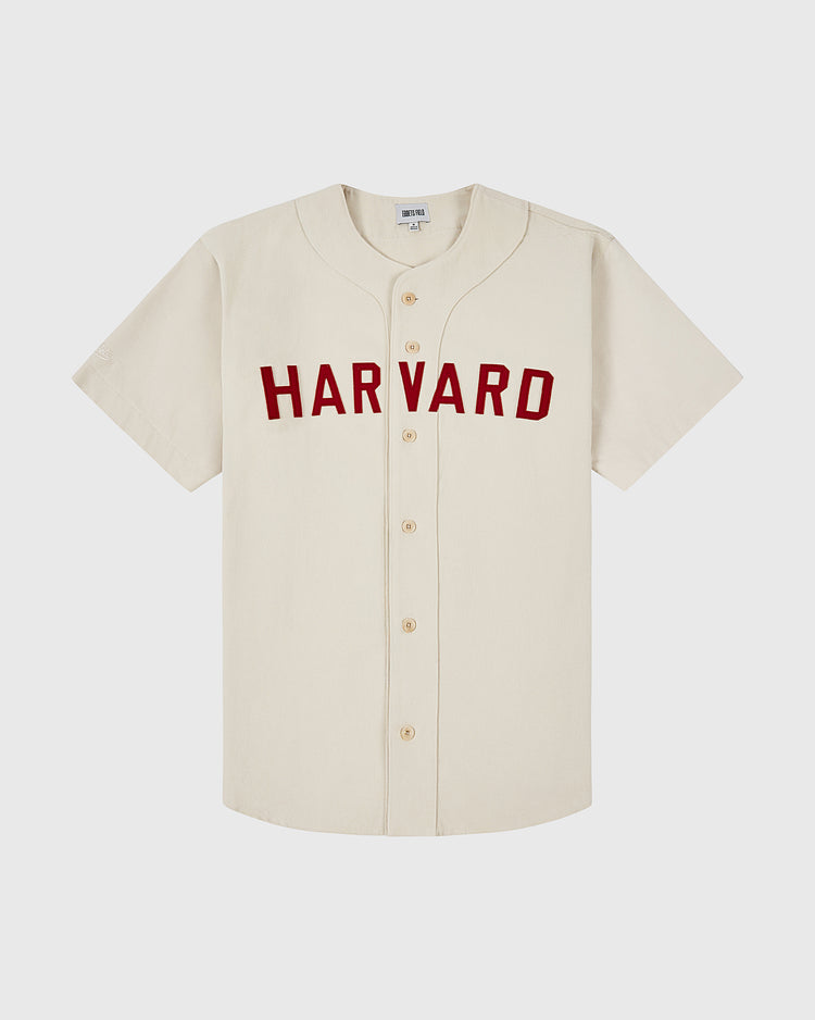 The Ebbets Field HARVARD COTTON TWILL JERSEY Natural is a cream-colored, short-sleeve button-up baseball jersey featuring bold red HARVARD lettering across the chest, shown on a plain white background.