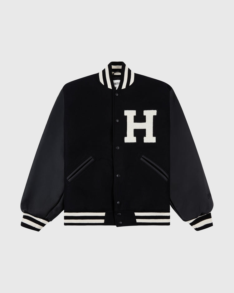 The Ebbets Field Harvard University Wool and Leather Varsity Jacket features black leather sleeves, white-striped ribbed trim, and a large white H on the chest—a modern take on the classic 1950s varsity style.