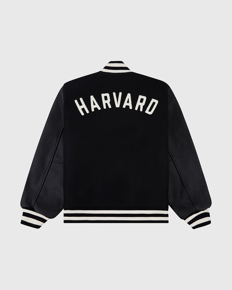The Ebbets Field Harvard University Wool and Leather Varsity Jacket features a black design with white striped cuffs, collar, and hem, plus bold white HARVARD lettering across the back in classic 1950s varsity style.