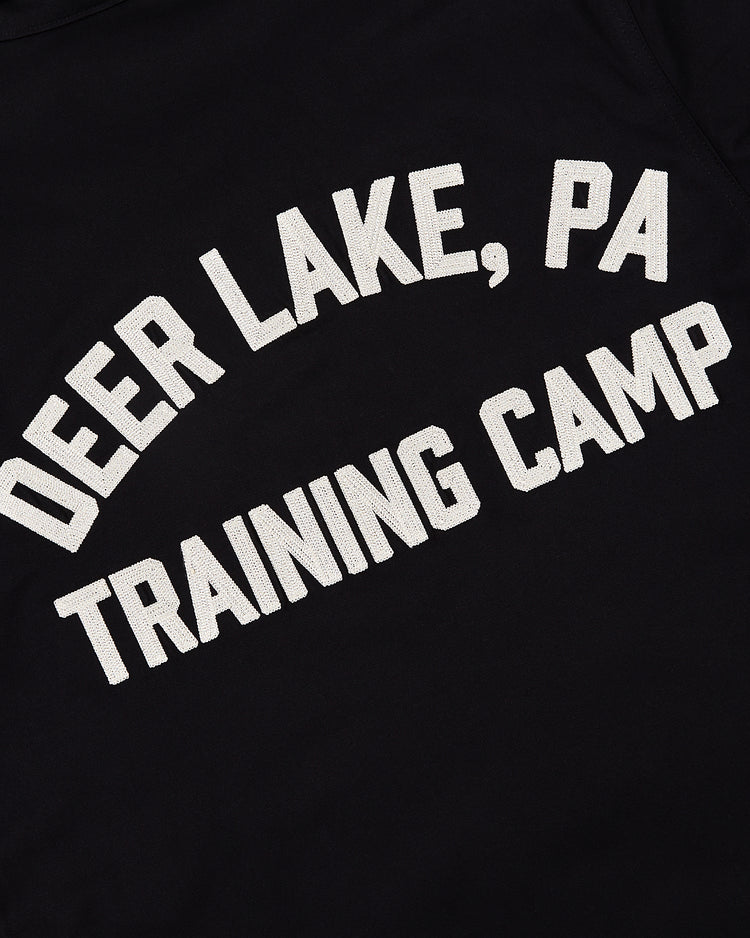 The Ebbets Field Muhammad Ali Training Camp Cotton Grounds Crew Jacket features white block letters on black fabric spelling DEER LAKE, PA TRAINING CAMP in an arch, inspired by Ali’s Fighter's Heaven gym workwear.