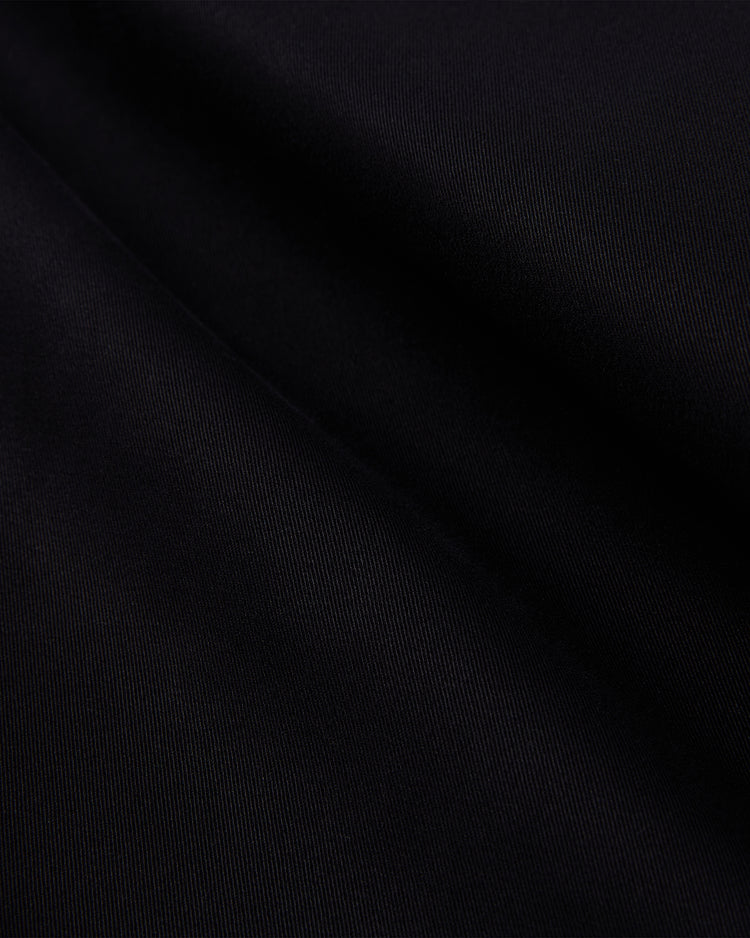 Close-up of soft black cotton with a subtle diagonal weave on the Ebbets Field Muhammad Ali Training Camp Grounds Crew Jacket, inspired by Ali’s workwear—gentle folds and shadows evoke the spirit of Fighter’s Heaven.