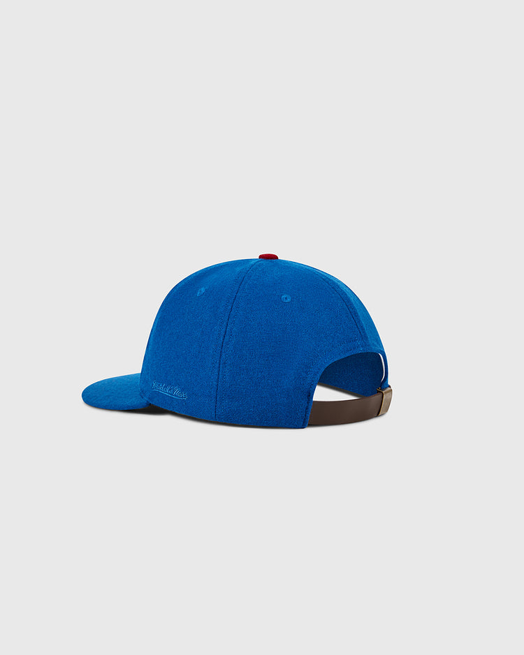 The Ebbets Field Chicago Cubs 1956 MLB Authentic Wool Ballcap is shown from the back and side, featuring a brown adjustable strap and a red top button, set against a plain light gray background.