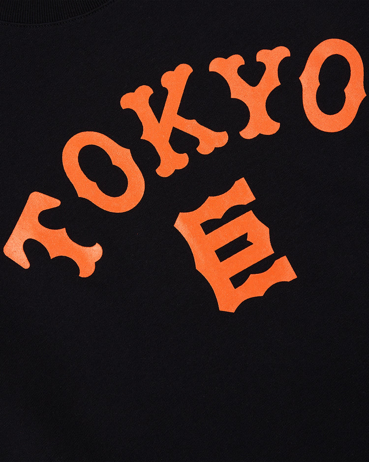 The Ebbets Field Tokyo Giants Short Sleeve Graphic Tee features black fabric with bold, curved orange 