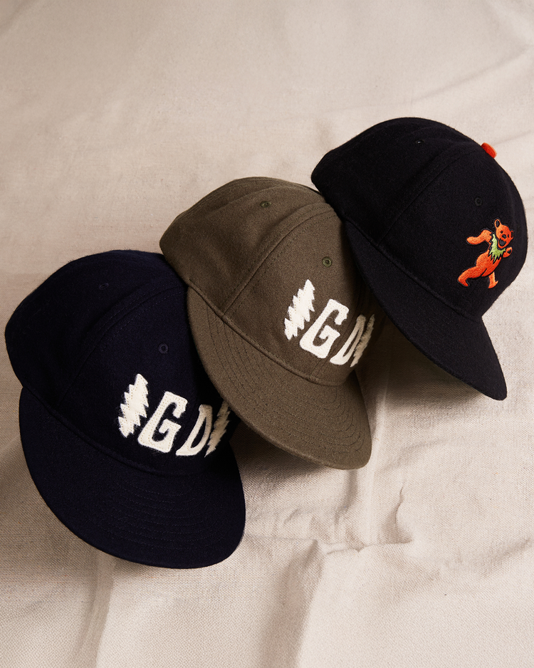 Three Ebbets Field Grateful Dead ballcaps sit side by side: a navy Double Bolt Wool Ballcap, an olive green 60th anniversary cap with GD and a lightning bolt, and a black cap with an orange dancing bear.