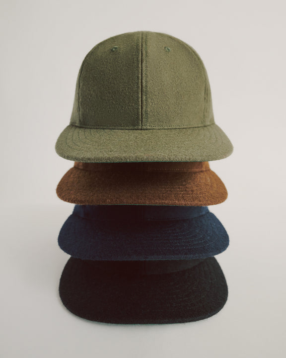 Four textured baseball caps, stacked vertically, in olive green, brown, navy blue, and black, against a plain white background.
