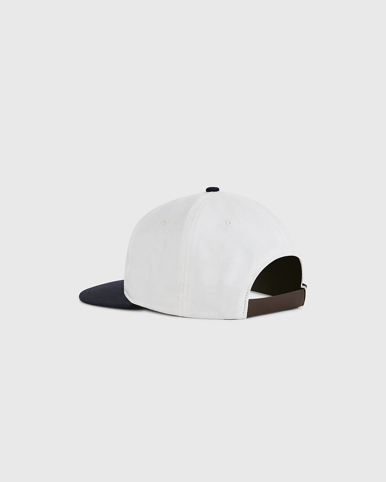 The Ebbets Field USA National Team Cotton Twill Ballcap is white with a black brim, shown angled from the back to display its adjustable strap. The background is plain and light gray.