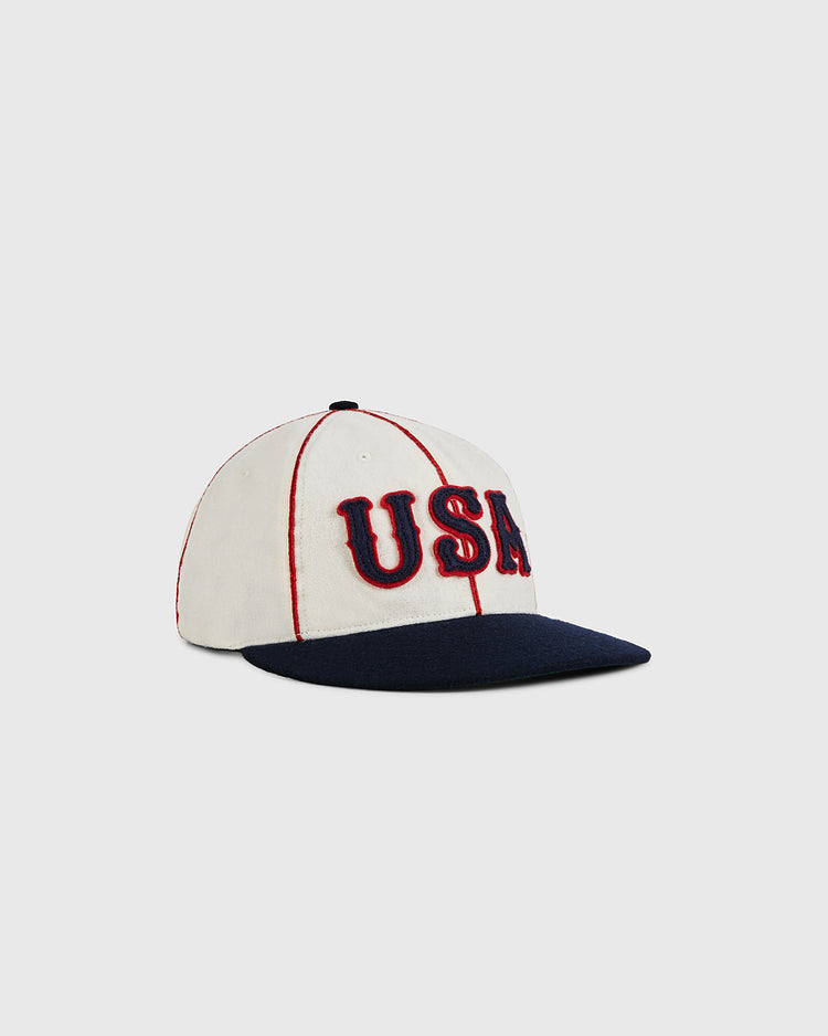 The Ebbets Field USA National Team 1936 Authentic Wool Ballcap features bold red and blue USA letters, red stitching accents, and a navy blue brim, evoking classic Olympic style, displayed against a plain light background.