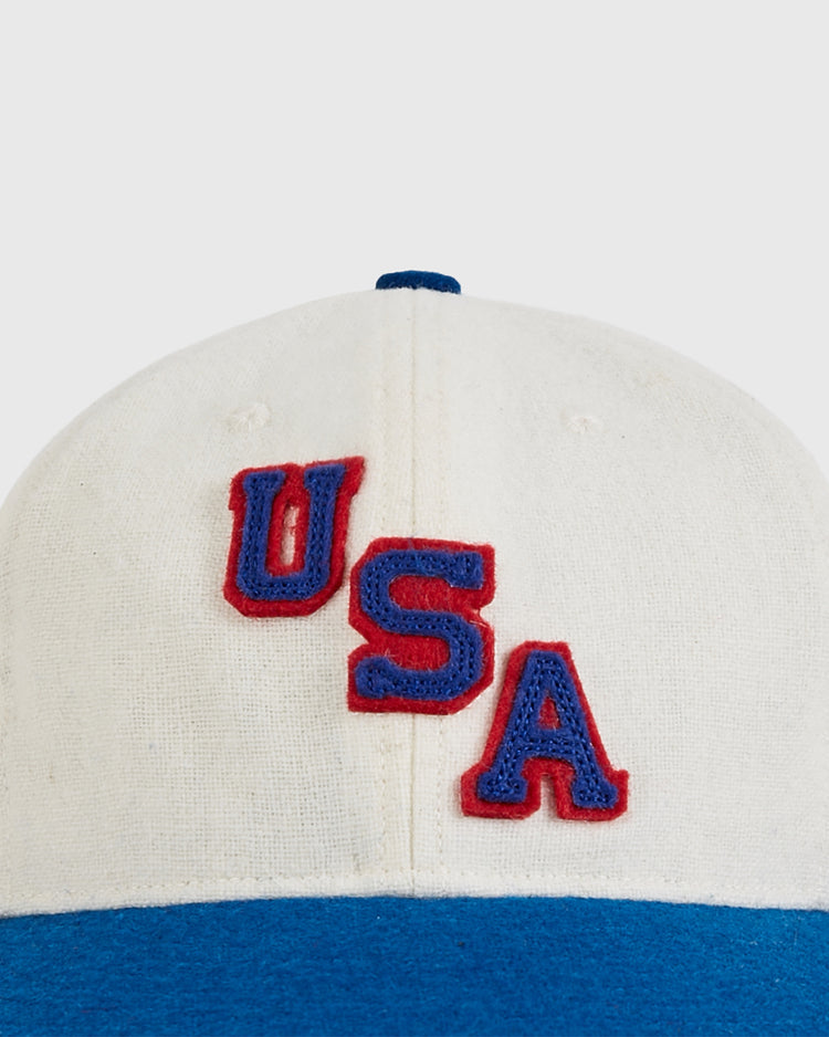 A close-up of the Ebbets Field USA 1960 Wool Ballcap, a white and blue baseball cap with bold red and blue 