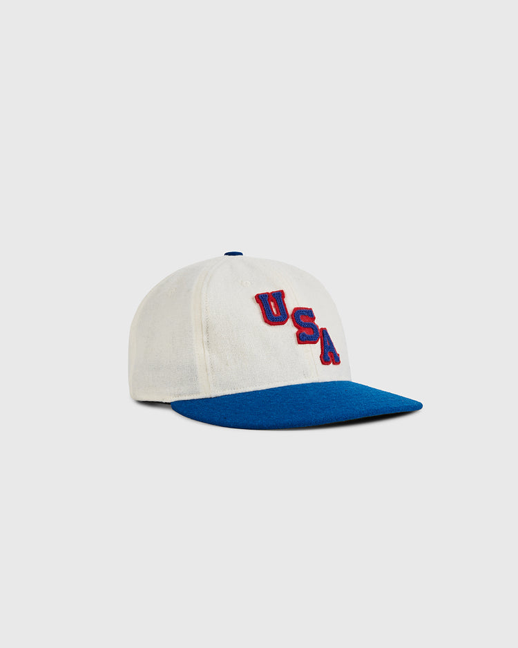 The Ebbets Field USA 1960 Wool Ballcap features a white crown, blue brim, and bold red USA lettering, channeling vintage Olympic hockey style. Its raised design stands out against a plain light background.