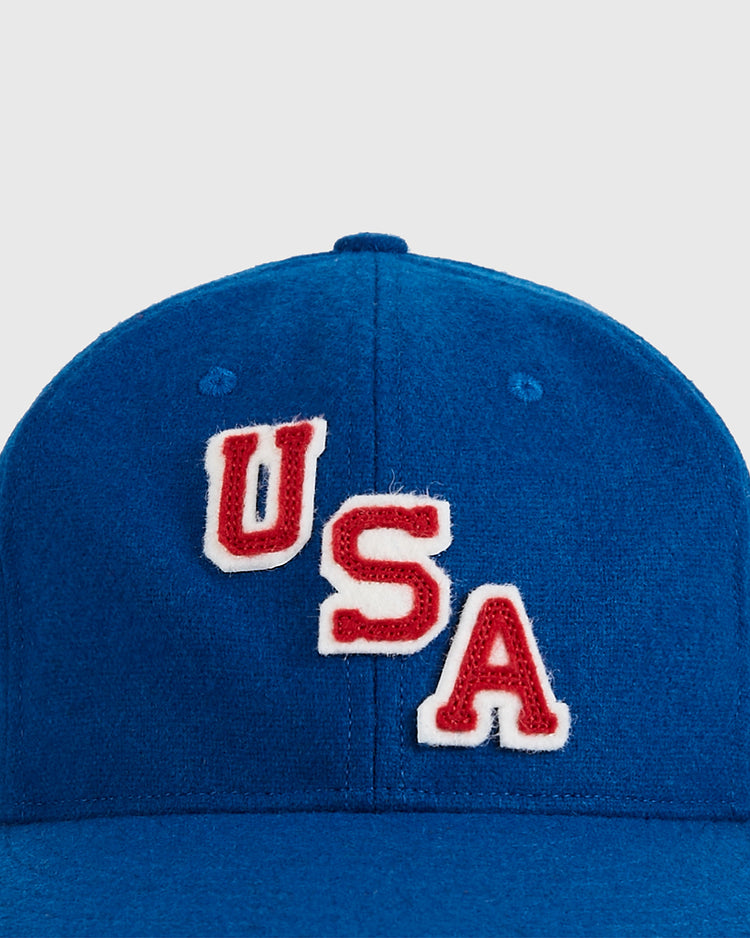 A close-up of the Ebbets Field USA 1960 Wool Ballcap—a vintage blue hat with bold red and white embroidered “USA” letters on the front, inspired by Miracle on Ice greatness.