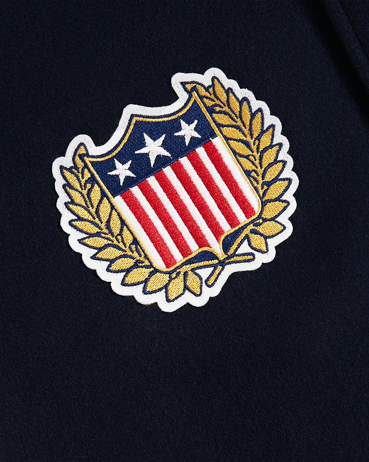 The Ebbets Field USA 1960 All-Wool Varsity Jacket features an embroidered shield patch with red and white stripes, three white stars on blue, and a gold laurel wreath on dark fabric, evoking classic vintage style.