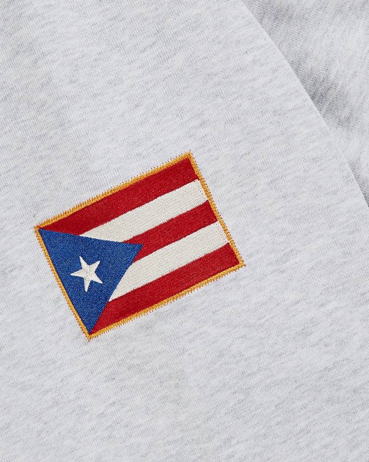 A close-up of a small Puerto Rican flag patch sewn onto the Ebbets Field Puerto Rico 1972 National Team Heavyweight Cotton Terry Pullover Hoodie in light gray.