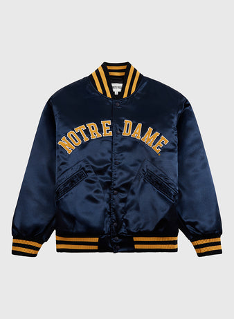 The Ebbets Field Notre Dame Satin Varsity Jacket features navy blue satin, bold yellow NOTRE DAME lettering, yellow and navy striped trim, and two diagonal front pockets for classic Fighting Irish style.