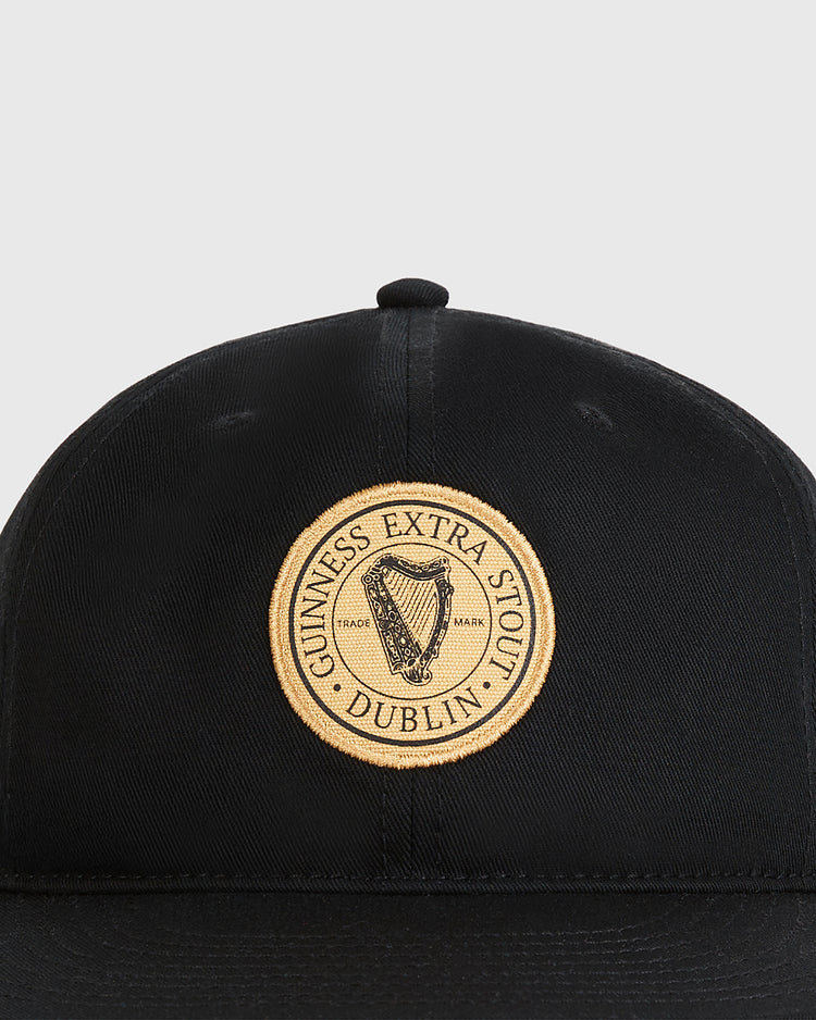The Ebbets Field Guinness Extra Stout Patch Cotton Twill Ballcap is a black cap with a round gold Guinness patch and harp logo on the front, inspired by vintage styles.