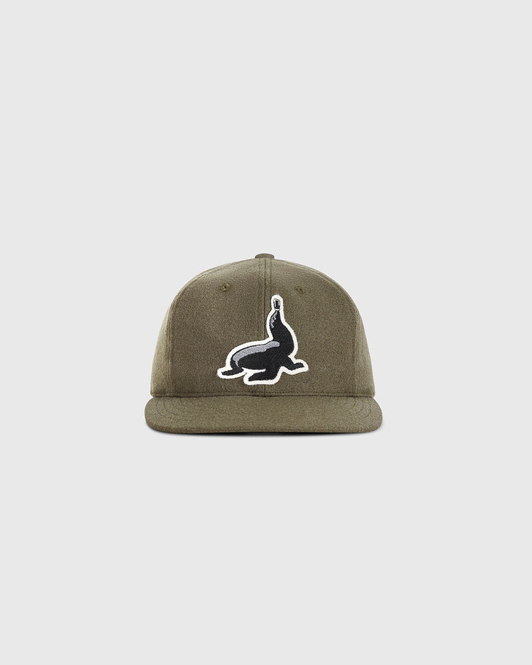 The Guinness Seal Authentic Wool Ballcap by Ebbets Field is a khaki green cap featuring a black and white seal balancing a ball patch on the front, shown against a plain white background.