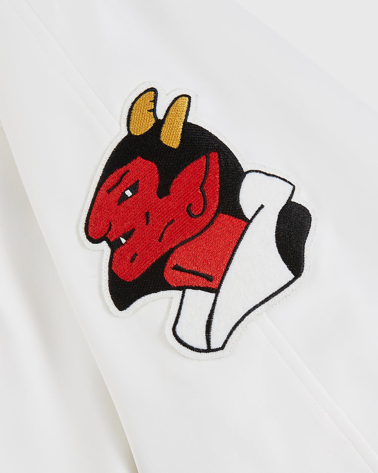 A red devil head patch with yellow horns and a white collar, inspired by the Diablos Rojos del Mexico Satin Varsity Jacket by Ebbets Field, is sewn onto a white fabric background.