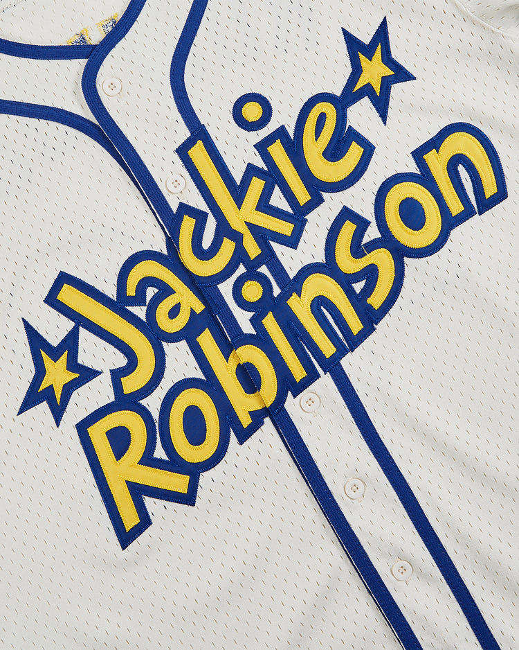 The Ebbets Field Jackie Robinson Comic Book Hero Mesh Baseball Jersey is white with blue trim and bold yellow-blue lettering, accented by stars—a tribute to the barrier-breaking baseball legend.