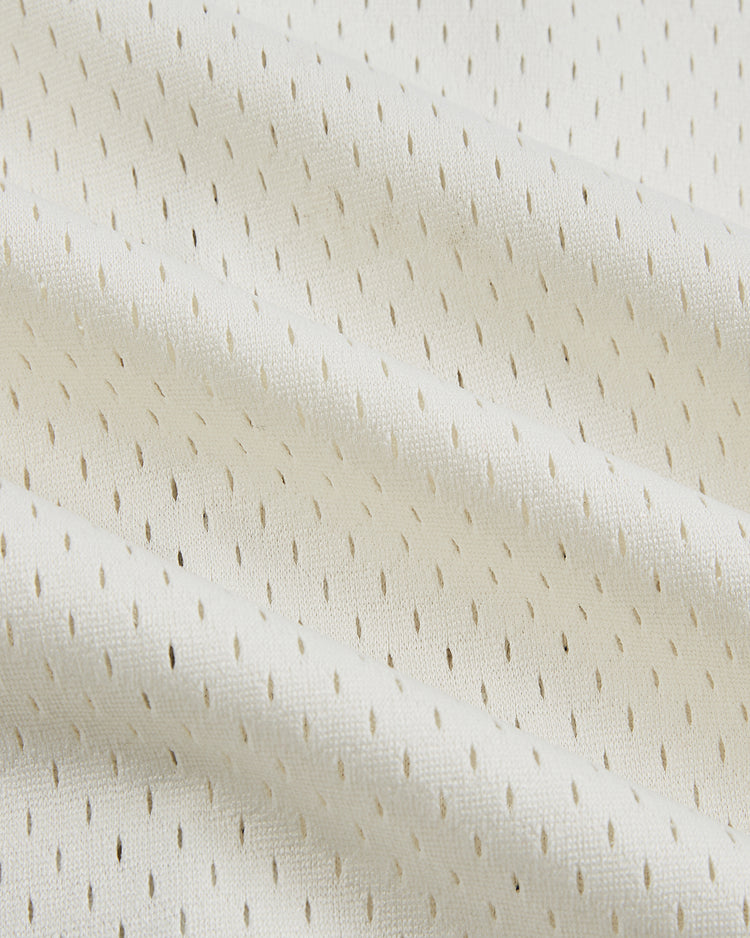 Close-up of off-white mesh fabric with small, evenly spaced holes and gentle folds, evoking the breathable texture of the Ebbets Field Jackie Robinson Comic Book Hero Mesh Baseball Jersey.