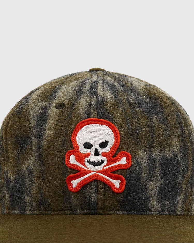 A close-up of the Ebbets Field Mossy Oak x Ebbets Field Sioux City Ghosts Ballcap, featuring Mossy Oak Bottomland camo and a front white skull and crossbones patch outlined in red.
