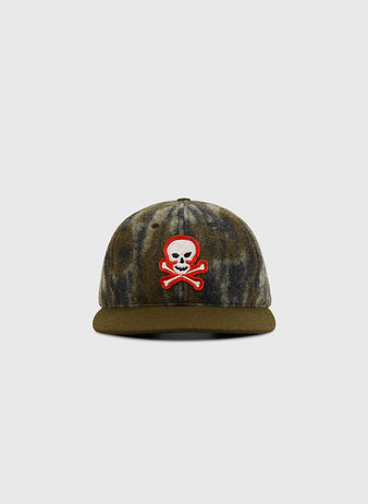 The Ebbets Field Mossy Oak x Sioux City Ghosts Ballcap features Mossy Oak Bottomland camo, a green brim, and a red, white, and black skull-and-crossbones patch on the front, displayed against a plain light gray background.