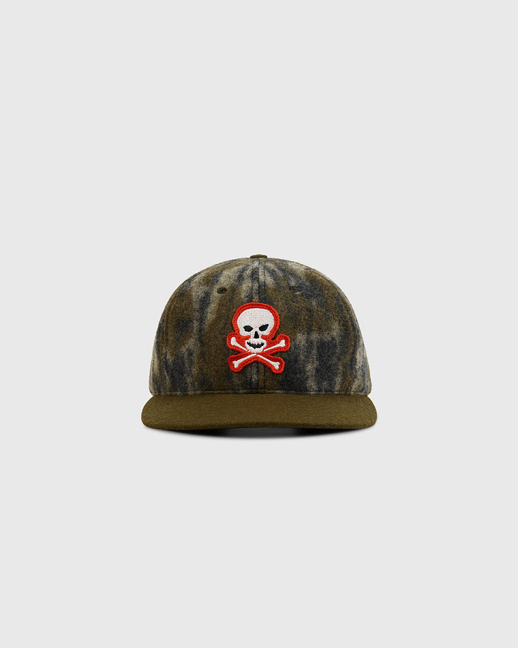 The Ebbets Field Mossy Oak x Sioux City Ghosts Ballcap features Mossy Oak Bottomland camo, a green brim, and a red, white, and black skull-and-crossbones patch on the front, displayed against a plain light gray background.