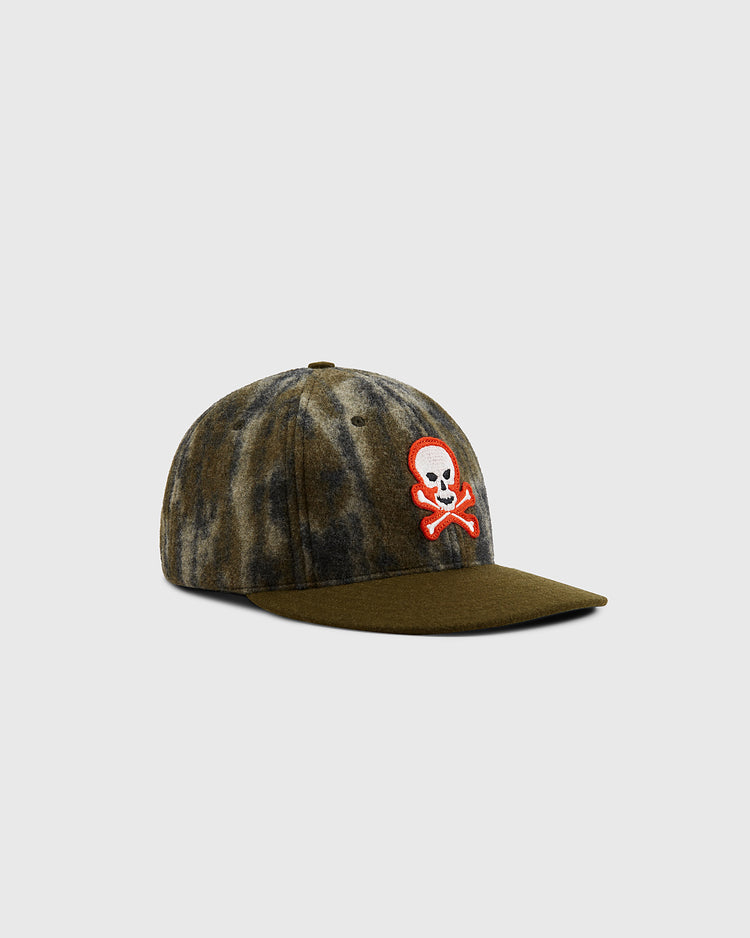 The Ebbets Field Mossy Oak x Sioux City Ghosts Ballcap features an olive green and brown tie-dye design with a red-outlined white skull and crossbones patch on the front, displayed on a plain light background.