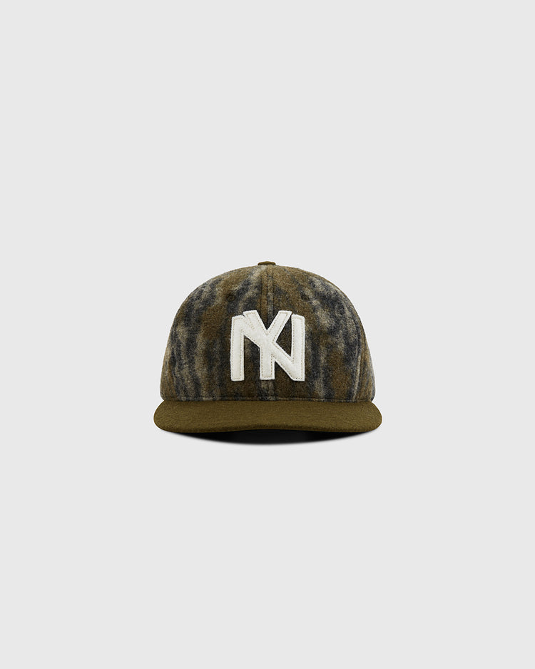 The Ebbets Field Mossy Oak x 1935 Brooklyn Eagles Ballcap features a Mossy Oak Bottomland camo design and a bold white NY logo on the front, shown on a plain gray background.