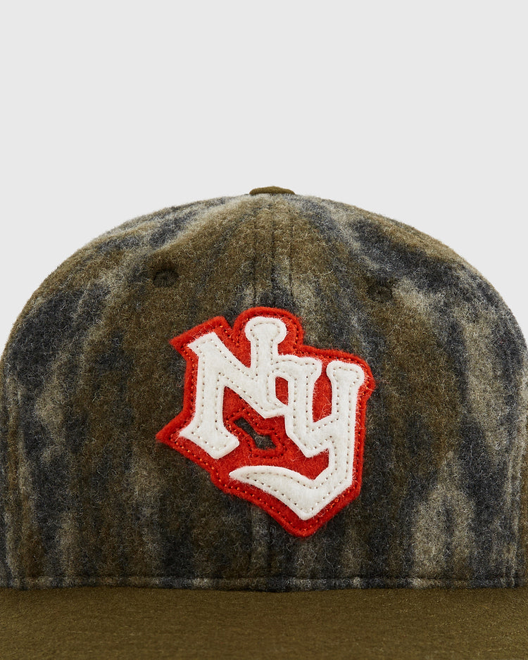 A close-up of the Mossy Oak x Ebbets Field New York Knights Ballcap, featuring brown and gray camo by Ebbets Field with a red and white embroidered NY logo on the front.
