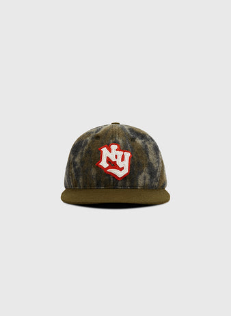 The Ebbets Field Mossy Oak x New York Knights Ballcap features a brown and gray camo pattern with a red and white NY logo on the front, displayed against a plain light gray background.