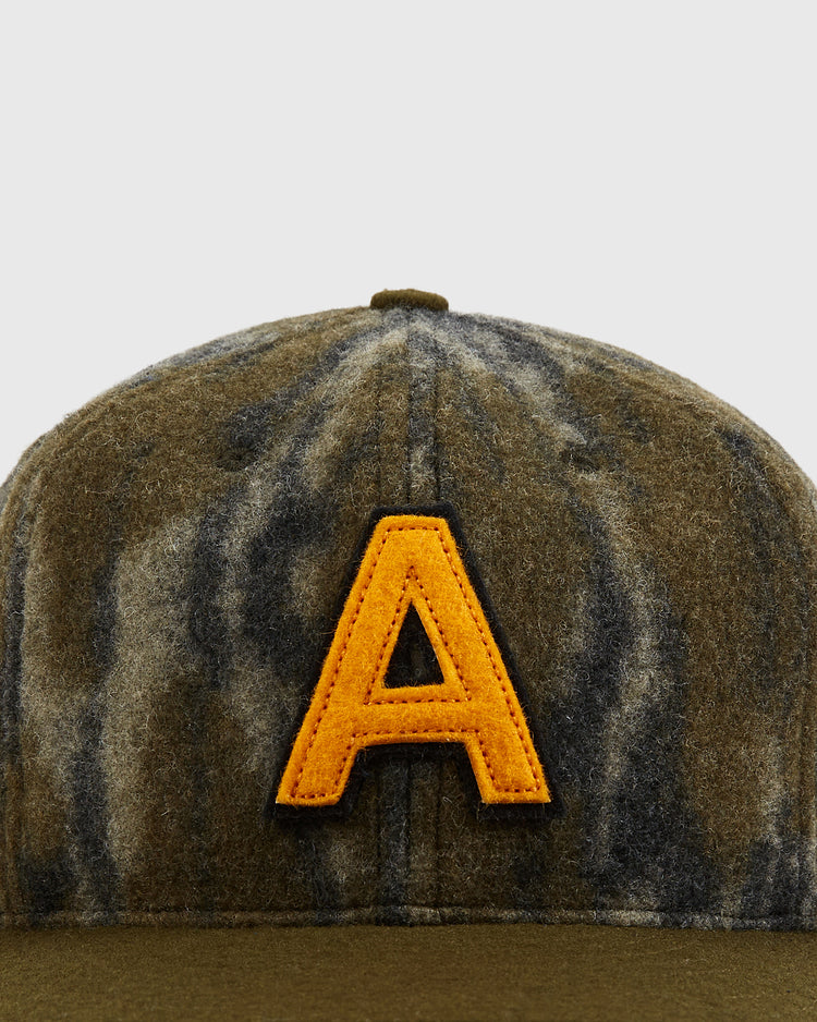 A close-up of the Ebbets Field Mossy Oak x Ebbets Field 1957 Army Ballcap, featuring a brown and gray marbled pattern inspired by Mossy Oak Bottomland camo and a bold yellow-orange letter A patch on the front, set against a plain light gray background.