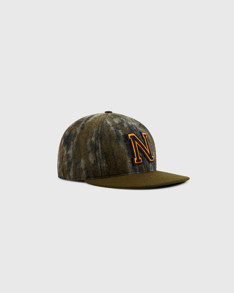 The Ebbets Field Mossy Oak x Ebbets Field 1947 Navy Ballcap features green and gray Bottomland Camo, a flat brim, and a bold yellow outlined N on the front, inspired by a classic Navy Academy cap, shown on a plain light gray background.