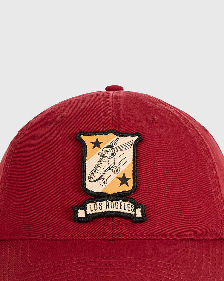 The Los Angeles Lincoln Park Roller Skating Rink Washed Cotton Ballcap by Ebbets Field is a vintage red cap with a gold patch featuring a classic airplane, black stars, diagonal stripes, and a 