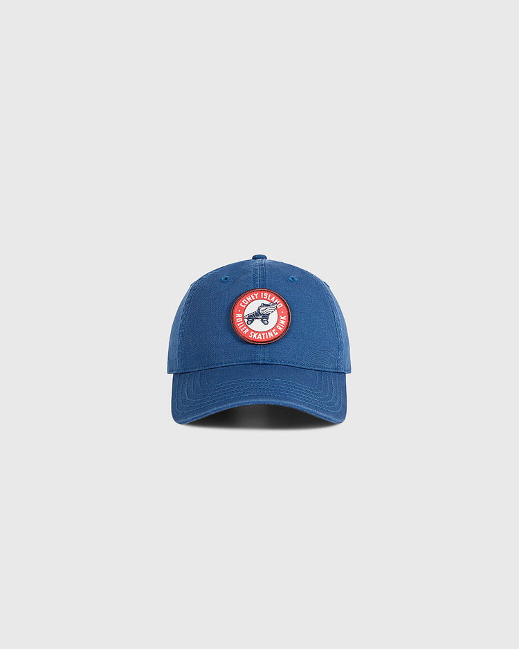 A washed cotton Coney Island Roller Skating Rink ballcap by Ebbets Field in blue, featuring a circular red and white patch on the front, set against a light gray background. Perfect for fans of Brooklyn style.