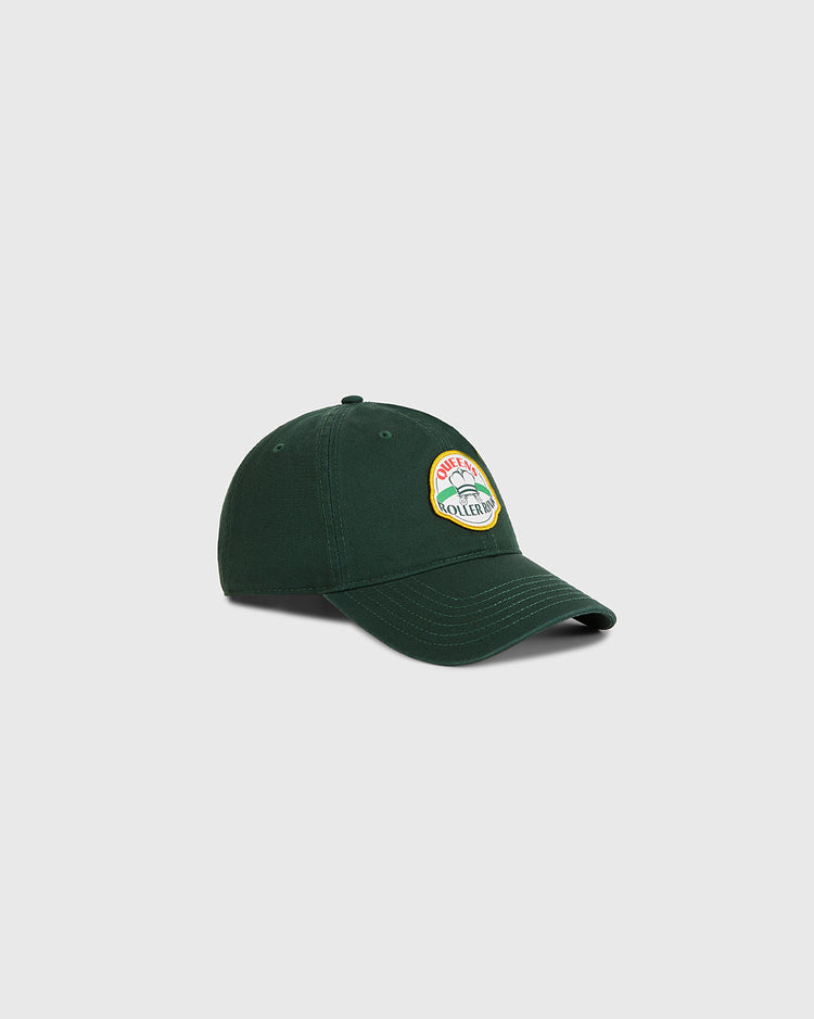 The Ebbets Field Queens Roller Rink Washed Cotton Ballcap in dark green features a colorful circular patch with text and a mountain graphic on the front, shown against a plain light gray background.