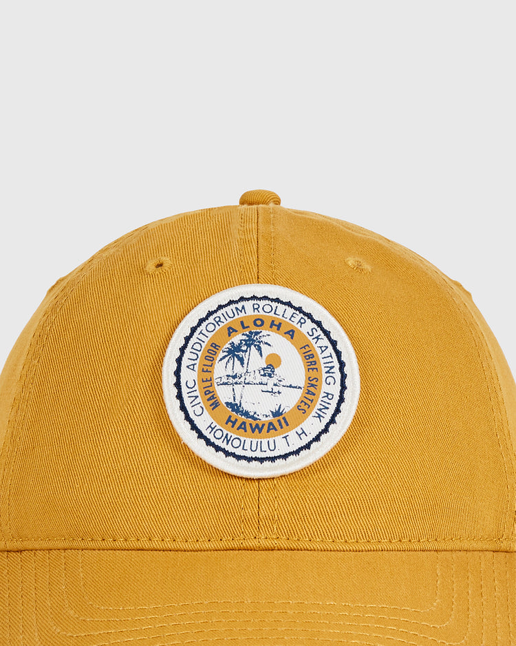 The Ebbets Field Hawaii Civic Auditorium Roller Rink Washed Cotton Ballcap features a mustard yellow vintage look and a round patch with a palm tree, sun, “Aloha Hawaii,” and “Civic Auditorium Roller Skating Rink, Honolulu T.H.”.