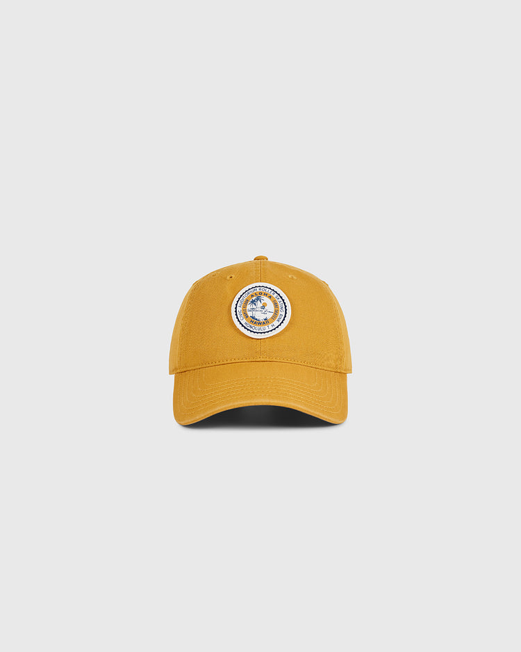 The Ebbets Field Hawaii Civic Auditorium Roller Rink Washed Cotton Ballcap in mustard yellow features a circular blue and white patch, inspired by the historic rink, shown against a plain light gray background.