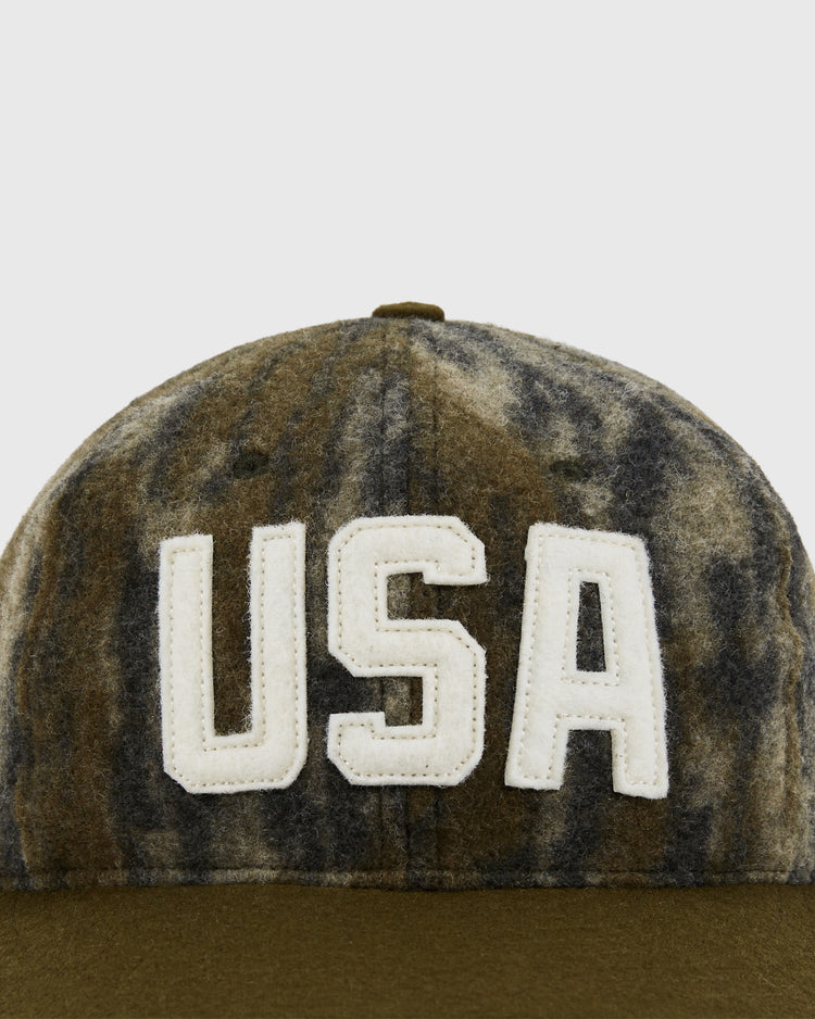 A close-up of the Mossy Oak x Ebbets Field 1956 USA National Team Ballcap by Ebbets Field, featuring a green and gray Bottomland Camo pattern with bold white 