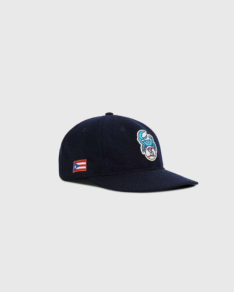 The Ebbets Field Santurce Cangrejeros Crab Wool Ballcap is a navy blue cap with an embroidered cartoon crab on the front and a small Puerto Rican flag patch on the side, shown against a light gray background.