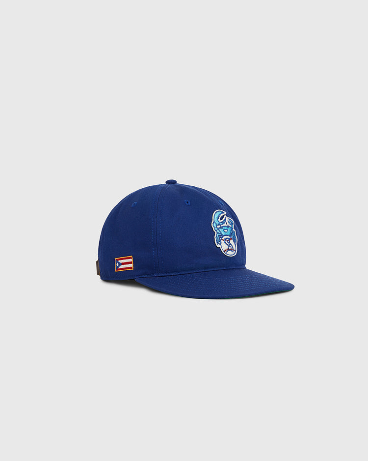 The Ebbets Field Santurce Cangrejeros Crab Cotton Twill Ballcap is a blue cap with front embroidery and a Puerto Rican flag patch on the side, celebrating Puerto Rican baseball, shown on a plain light gray background.