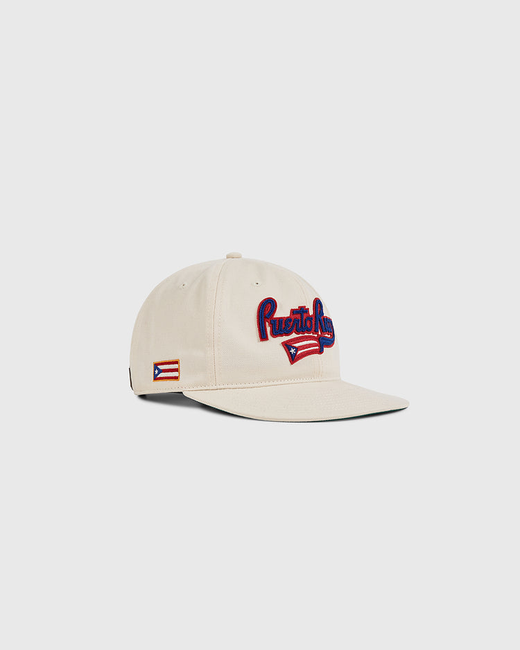 The Ebbets Field Puerto Rico 1972 National Team Cotton Twill Ballcap features “Puerto Rico” embroidered in red and blue on beige cotton twill, with a Puerto Rican flag patch on the side brim. Shown against a plain white background.