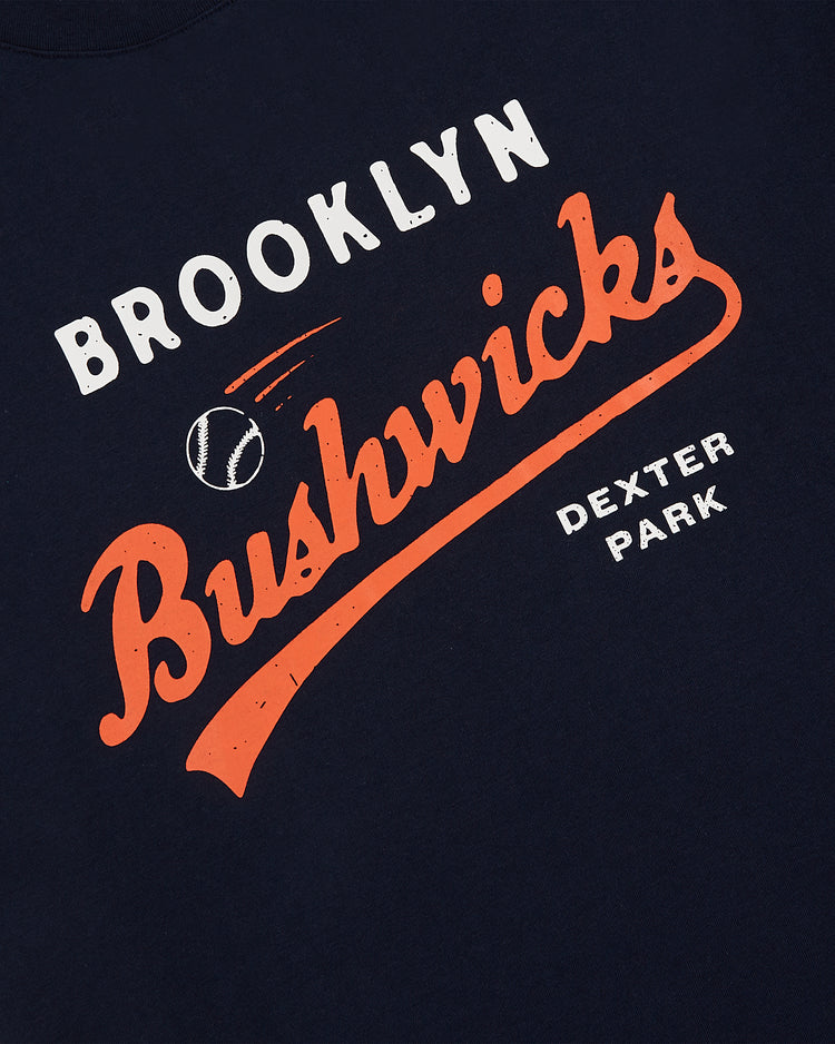 The Brooklyn Bushwicks Short Sleeve Graphic Tee by Ebbets Field is a navy blue vintage-style shirt with white and orange 