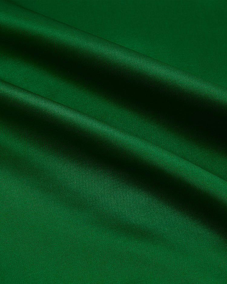 Close-up of smooth, emerald green satin fabric with soft diagonal folds, evoking the vintage style of EFF’s Kansas City Athletics 1963 Satin Windbreaker Jacket and showcasing its shiny, reflective surface.