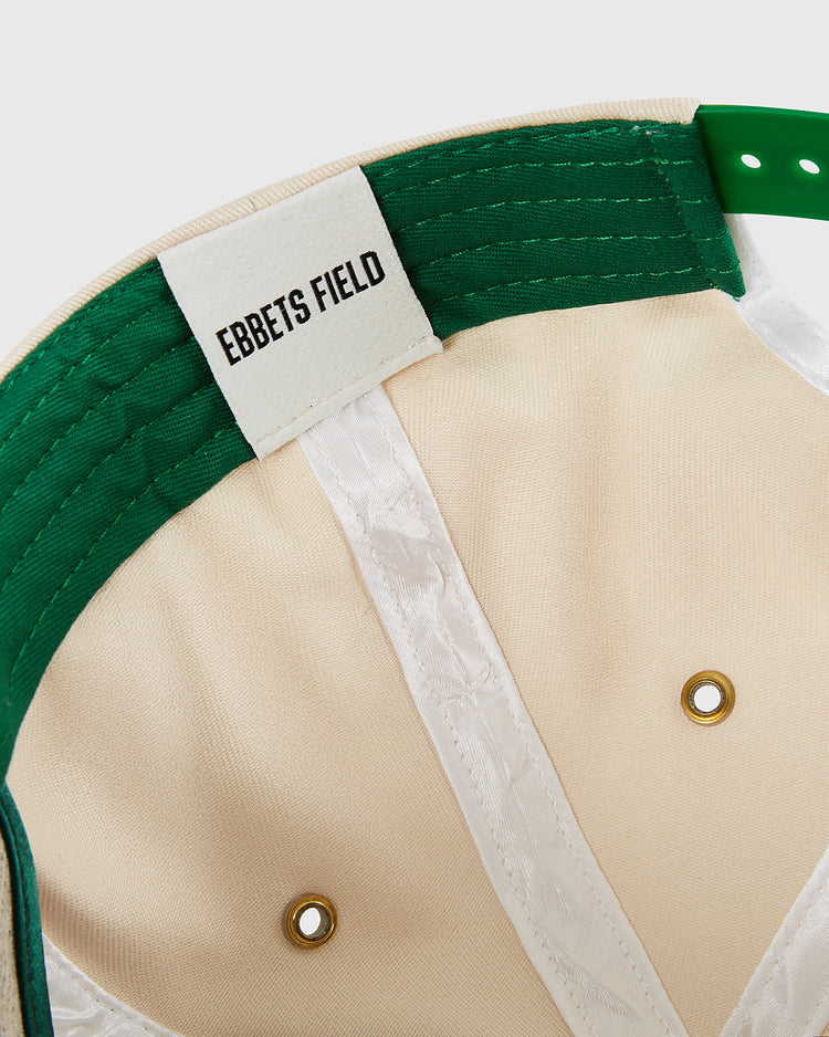 Close-up of the inside of the New York Cosmos A-Frame Cotton Twill Ballcap by Ebbets Field, showing a label sewn onto a white band and two gold ventilation eyelets in this classic beige and green snapback.