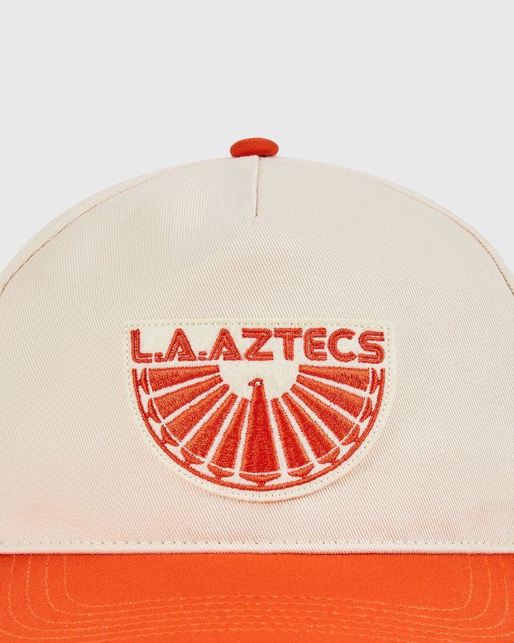 The Ebbets Field Los Angeles Aztecs A-Frame Cotton Twill Ballcap features a beige and orange design with an embroidered red L.A. Aztecs logo and sunburst, ideal for any Aztecs hat collector.