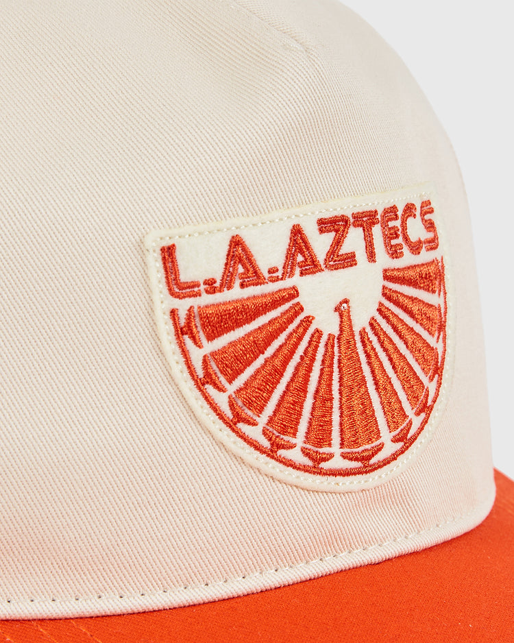 Close-up of the Los Angeles Aztecs A-Frame Cotton Twill Ballcap by Ebbets Field in white with an orange brim, featuring an embroidered 