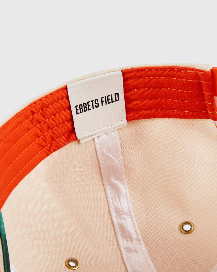 A close-up of the Los Angeles Aztecs A-Frame Cotton Twill Ballcap by Ebbets Field shows an orange sweatband, a white Ebbets Field tag, and two brass eyelets on the crown, reflecting the quality of this North American Soccer League cap.